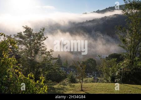 Am frühen Morgen bedeckt der Nebel das Dorf Saint-Étienne-de-Baïgorry, von der Landstraße aus gesehen, die zum Col d'Izpégi, Frankreich, führt Stockfoto