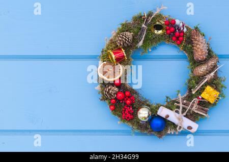 Weihnachtskranz. Fichtenzweige mit Dekoration hängen an einer blauen Holzwand Stockfoto