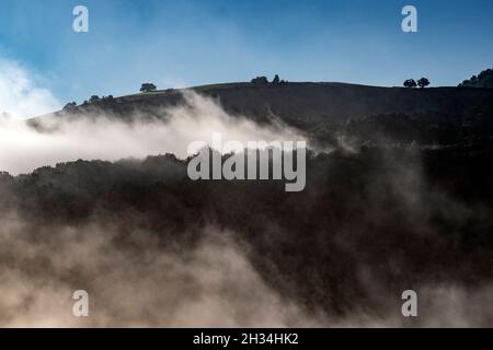 Am frühen Morgen bedeckt der Nebel das Dorf Saint-Étienne-de-Baïgorry, von der Landstraße aus gesehen, die zum Col d'Izpégi, Frankreich, führt Stockfoto