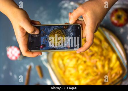 Ein Koch fotografiert einen frisch gebackenen Thanksgiving-Apfelkuchen auf dem Smartphone. Kochen, Süßes zu Hause backen. Herbstliche hausgemachte Süßigkeiten, Tarte oder cak Stockfoto