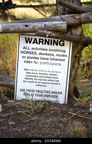 Ein Schild warnt vor möglichen Gefahren von Aktivitäten mit Pferden im lebenden Geschichtsmuseum El Rancho de las Golondrinas in Santa Fe, New Mexico. Stockfoto