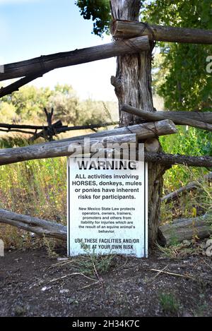 Ein Schild warnt vor möglichen Gefahren von Aktivitäten mit Pferden im lebenden Geschichtsmuseum El Rancho de las Golondrinas in Santa Fe, New Mexico. Stockfoto