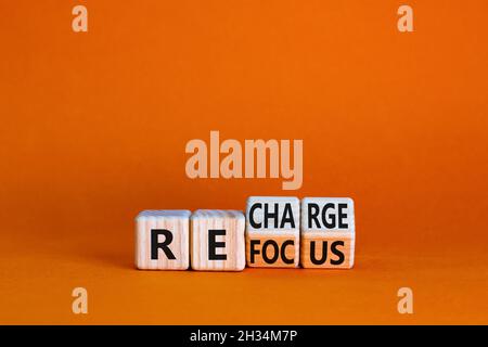 Symbol erneut fokussieren und aufladen. Geschäftsmann drehte Würfel und änderte das Wort „Fokus“ in „aufladen“. Schöner orangefarbener Tisch, orangefarbener Hintergrund. Unternehmen Stockfoto