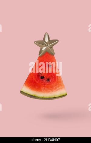 Weihnachtsbaum aus Wassermelone und Weihnachtsstern auf rosa Hintergrund. Minimales Urlaubskonzept. Weihnachtsbaum aus Lebensmitteln. Stockfoto