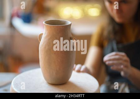 Kreativer Prozess beim Töpferunterricht: Handgefertigter Töpferkrug auf dem Tisch im Atelier mit weiblicher Keramikerin Stockfoto