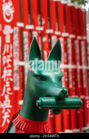 Eine Statue der Inari Kitsune oder Fuchsgöttin, die ein rotes Lätzchen trägt und von Nobori-Bannern umgeben ist, am Toyokawa Inari Betsuin Tempel in Asakusa, Tokio, Japan. Der buddhistische Tempel ist Teil der Soto Zen Sekte und beherbergt die Gottheit Toyokawa Dakinishinten, aber auch bekannt für die Tausenden von Fuchsstatuen. Stockfoto