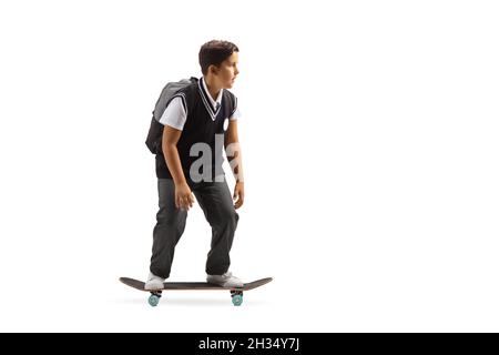 Ganzkörperaufnahme eines Schuljungen in einer Uniform, der auf weißem Hintergrund auf einem Skateboard fährt Stockfoto