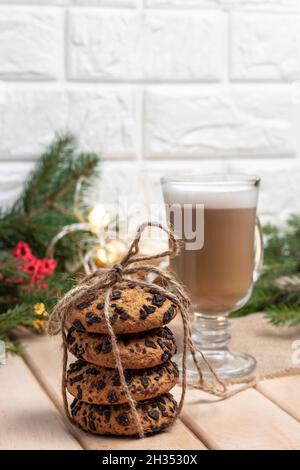 Weihnachts-Haferkekse mit Schokolade mit warmem hausgemachtem Cappuccino auf Holzbrettern und Christbaumzweigen mit runden Laternen. Stockfoto