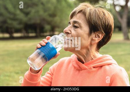 Ältere Frau trinkt nach dem Sport Jogging-Routine im Freien im Stadtpark - ältere Menschen trainieren und gesund leben Stockfoto