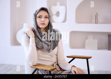 Weiße Frau im Kopftuch sitzt auf einem Stuhl in der Lounge. Stockfoto
