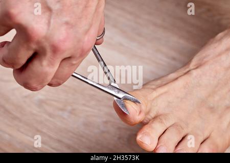 Der Mensch schneidet Nägel, während er sich Pediküre macht. Stockfoto