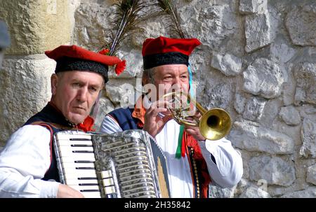 Zwei ältere polnische Männer in traditionellen polnischen Outfits spielen Akkordeon und Trompete auf der Straße in der Altstadt von Krakau, Polen. Stockfoto