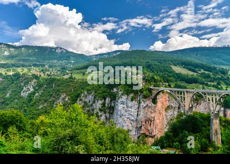 Große, dramatische Wolken, die sich gegen einen tiefblauen Himmel erheben, und die beeindruckend hohe Durdevica Tara Brücke in der Durmitor Region im Norden Montenegros. Stockfoto