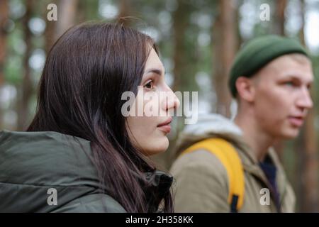 Eine junge Frau und ein Mann vor den unscharfen Bäumen. Ein heterosexuelles Paar. Menschen, die durch einen herbstlichen Park oder Wald schlendern. Selektiver Fokus. Stockfoto