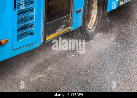 Blauer Stadtbus, der auf einer regnerischen Straße mit Wasserspritzern fährt Stockfoto