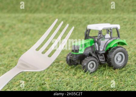 Kleiner Spielzeugschlepper auf faux/fake Gras mit Edelstahlgabelzinken. Für die britische Lebensmittelproduktion: Farm to Fork, Field to Fork / Field to Plate Idiome. Stockfoto