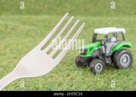 Kleiner Spielzeugschlepper auf faux/fake Gras mit Edelstahlgabelzinken. Für die britische Lebensmittelproduktion: Farm to Fork, Field to Fork / Field to Plate Idiome. Stockfoto