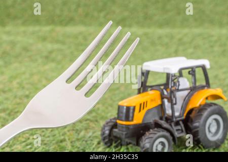 Kleiner Spielzeugschlepper auf faux/fake Gras mit Edelstahlgabelzinken. Für die britische Lebensmittelproduktion: Farm to Fork, Field to Fork / Field to Plate Idiome. Stockfoto