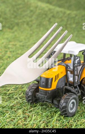 Kleiner Spielzeugschlepper auf faux/fake Gras mit Edelstahlgabelzinken. Für die britische Lebensmittelproduktion: Farm to Fork, Field to Fork / Field to Plate Idiome. Stockfoto