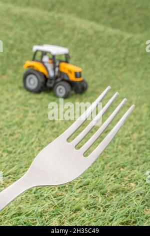 Kleiner Spielzeugschlepper auf faux/fake Gras mit Edelstahlgabelzinken. Für die britische Lebensmittelproduktion: Farm to Fork, Field to Fork / Field to Plate Idiome. Stockfoto