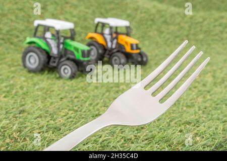 Kleiner Spielzeugschlepper auf faux/fake Gras mit Edelstahlgabelzinken. Für die britische Lebensmittelproduktion: Farm to Fork, Field to Fork / Field to Plate Idiome. Stockfoto