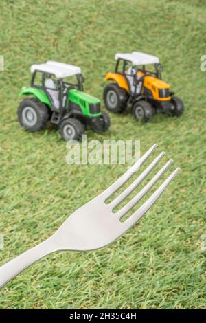 Kleiner Spielzeugschlepper auf faux/fake Gras mit Edelstahlgabelzinken. Für die britische Lebensmittelproduktion: Farm to Fork, Field to Fork / Field to Plate Idiome. Stockfoto
