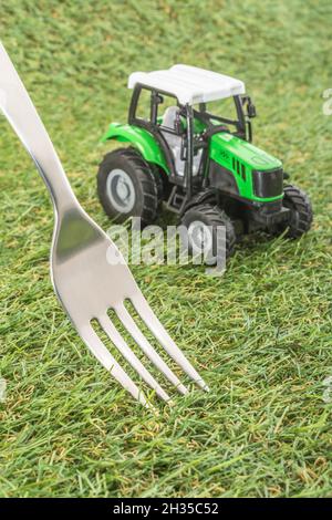 Kleiner Spielzeugschlepper auf faux/fake Gras mit Edelstahlgabelzinken. Für die britische Lebensmittelproduktion: Farm to Fork, Field to Fork / Field to Plate Idiome. Stockfoto