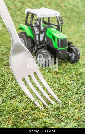 Kleiner Spielzeugschlepper auf faux/fake Gras mit Edelstahlgabelzinken. Für die britische Lebensmittelproduktion: Farm to Fork, Field to Fork / Field to Plate Idiome. Stockfoto