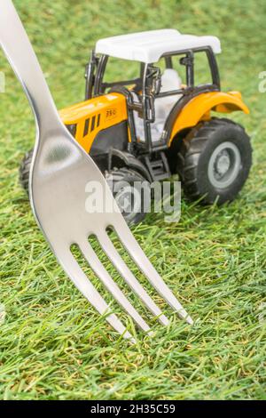 Kleiner Spielzeugschlepper auf faux/fake Gras mit Edelstahlgabelzinken. Für die britische Lebensmittelproduktion: Farm to Fork, Field to Fork / Field to Plate Idiome. Stockfoto