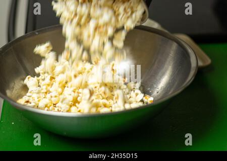 Gießen Sie frisch zubereitetes heißes Popcorn in eine Edelstahlschüssel Stockfoto