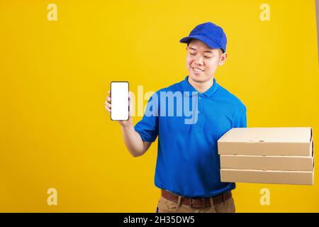 Aufgeregt Lieferservice Mann lächelnd trägt blaue Uniform halten Papierbehälter für Mitnehmen Pizzakartons Paket und zeigen Smartphone leeren Bildschirm, Stud Stockfoto