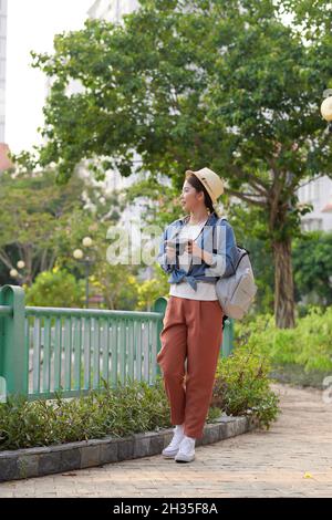 Junge schöne asiatische Rucksack Reisende Frau mit digitalen Kompaktkamera und Lächeln, Blick auf Copy Space Stockfoto