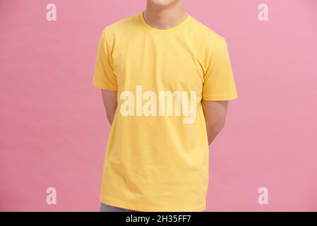 Teilansicht eines Mannes in gelbem T-Shirt, der die Hände hinter dem Rücken hält, isoliert auf rosa Stockfoto