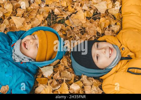 Kinder liegen auf gelben Blättern auf dem Boden. Jungen in Jacke, streut Blätter in einem Herbstpark. Das Kind freut sich über die Herbstblätter. Die Jungs sind es Stockfoto