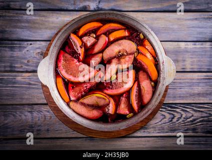 Großer Kessel Topf mit traditionellen heiß dampfenden Weihnachtsgetränk Glühwein rot gewürzt Gluhwein kocht mit Äpfeln und Zitrusfrüchten auf Holzgrund. Christus Stockfoto