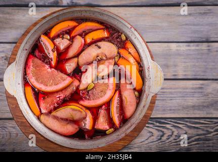 Großer Kessel Topf mit traditionellen heiß dampfenden Weihnachtsgetränk Glühwein rot gewürzt Gluhwein kocht mit Äpfeln und Zitrusfrüchten auf Holzgrund. Christus Stockfoto