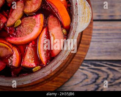 Großer Kessel Topf mit traditionellen heiß dampfenden Weihnachtsgetränk Glühwein rot gewürzt Gluhwein kocht mit Äpfeln und Zitrusfrüchten auf Holzgrund. Christus Stockfoto