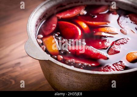 Großer Kessel Topf mit traditionellen heiß dampfenden Weihnachtsgetränk Glühwein rot gewürzt Gluhwein kocht mit Äpfeln und Zitrusfrüchten auf Holzgrund. Christus Stockfoto