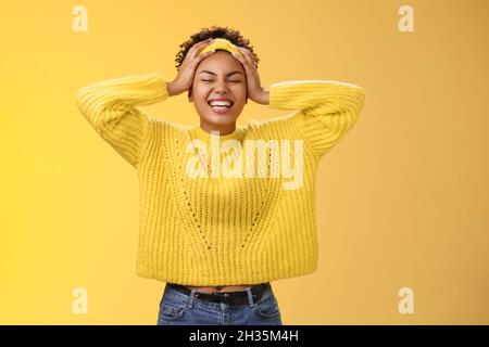 Sorglos glücklich glücklich afrikanisches Mädchen in Pullover Stirnband berühren Kopf mit Spaß lächeln erleichtert aufgeregt lachen laut nahe Augen jubeln verbringen Stockfoto