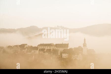 Arnsberg, Deutschland. Oktober 2021. Die historische Altstadt von Arnsberg im Sauerland mit ihrem markanten Glockenturm ist bei Sonnenaufgang am frühen Morgen von Nebel umgeben. Quelle: Julian Stratenschulte/dpa/Alamy Live News Stockfoto