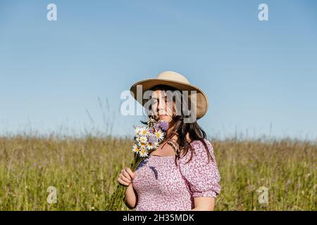 Porträt einer schönen jungen Frau, die auf dem Feld oder auf der Wiese steht und riecht nach Wildblumen Stockfoto