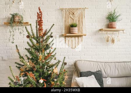 Weihnachten und Neujahr Dekorationen in modernem Wohndesign mit Sofa und Macrame-Paneelen. Boho-Design. Weihnachtsbaum geschmückt mit dr Stockfoto