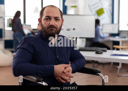Porträt eines gelähmten Geschäftsmannes im Rollstuhl, der im Startup-Büro in die Kamera schaut. Leitender Manager mit Behinderung, der für Geschäftspartnerschaft am Marketingunternehmen-Projekt arbeitet Stockfoto
