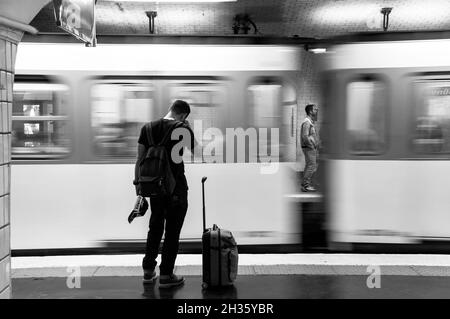 Paris (Frankreich): Atmosphäre im Untergrund. Der Reisende wird von hinten mit einem Koffer entlang eines Bahnsteigs in einer U-Bahn-Station und einem Zug in Bewegung gesehen Stockfoto