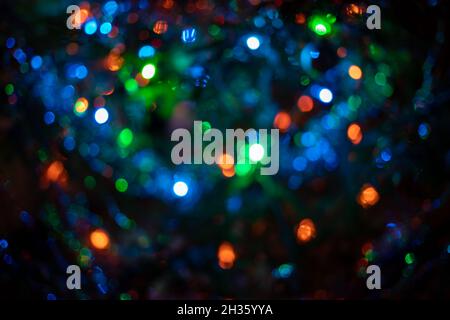 Unscharf verwischte Weihnachtsbaumgirlanden blau-grüne Farbe auf dunklem Hintergrund. Wunderschönes, vielfarbiger Bokeh. Stockfoto