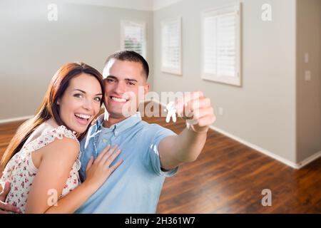 Junges Militärpaar zeigt die Hausschlüssel im leeren Raum des neuen Heims. Stockfoto