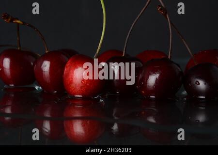 Kirschen, mit Wassertropfen auf schwarzem Hintergrund mit Spiegelung Stockfoto