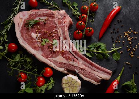 Fresh Raw Beef Bone Rib Steak auf schwarzem Brett mit Kräuter und Gewürze Stockfoto