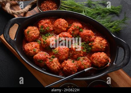 Boulettes de Poisson, gebratene Fischbälle in Tomatensauce in einer schwarzen Schale auf einem Betontisch mit Zutaten Stockfoto