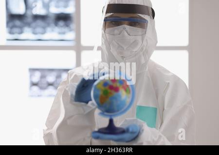 Arzt in schützendem medizinischen Anzug und Brille, die den Globus mit Coronavirus hält Stockfoto